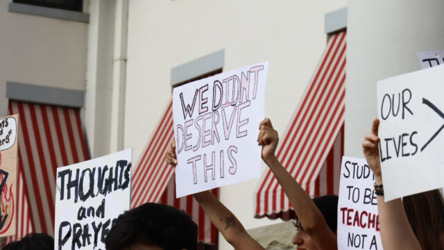 Students hold signs at a rally following a mass shooting; in the center of the image, a person holds a sign that reads 