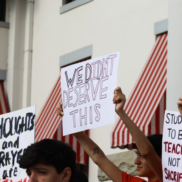 Students hold signs at a rally following a mass shooting; in the center of the image, a person holds a sign that reads 