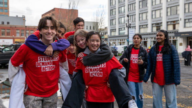 Students Demand Action volunteers pose for a group photo. Two students are being piggy-backed by two others. All are wearing red Students Demand Action t-shirts.