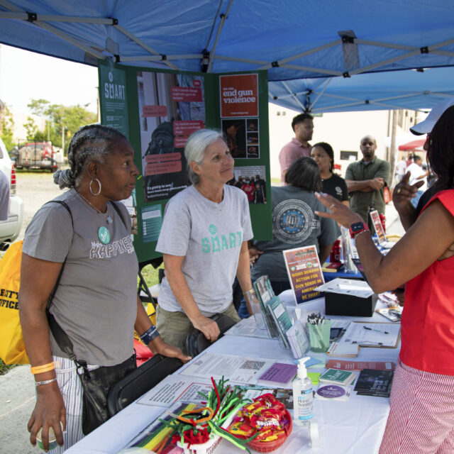 Three Be SMART volunteers talk about secure gun storage while tabling at a community event.