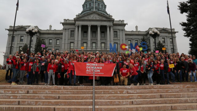 Moms Demand Action volunteers pose for a photo and hold up a Moms Demand Action banner on the steps of the Colorado State Capitol