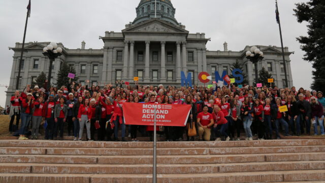 Moms Demand Action volunteers pose for a photo and hold up a Moms Demand Action banner on the steps of the Colorado State Capitol