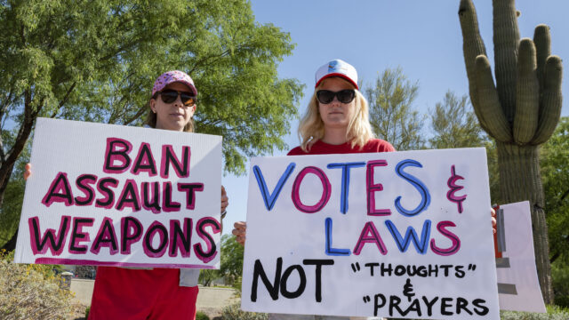 Moms Demand Action volunteers hold “Ban Assault Weapons” and “Votes & Laws, Not 'Thoughts & Prayers'” signs