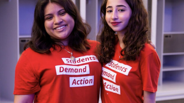 Ashley Castillo poses for a photo with another Students Demand Action volunteer. They are both wearing red Students Demand Action t-shirts.