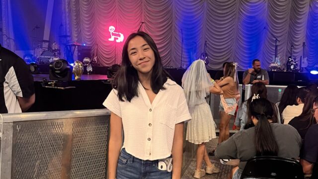 A teenage girl wears a white, button-up casual shirt with short sleeves. She also wears cut-off blue denim shorts. She has shoulder-length dark hair.