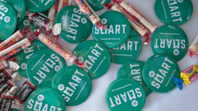 A pile of Be SMART buttons lay on a table at an event