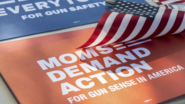 A red Moms Demand Action sign with a small American flag resting on top of the sign.