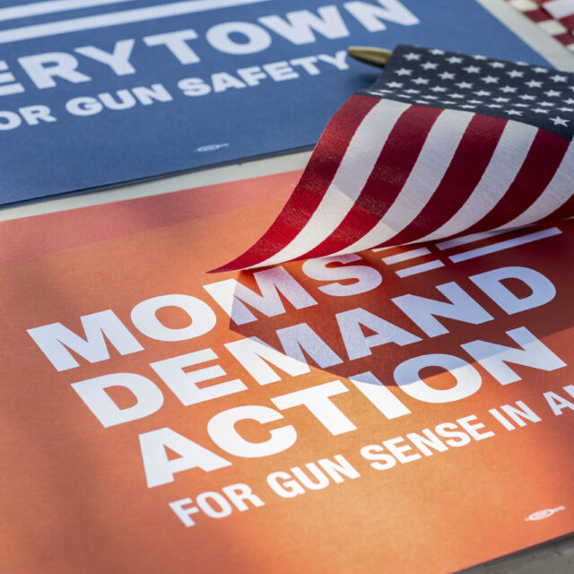 A red Moms Demand Action sign with a small American flag resting on top of the sign.
