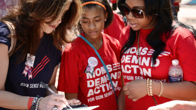 Three volunteers in Moms Demand Action and Gun Sense Voter shirts look at a clipboard together