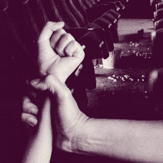 A magenta-hued textured graphic in which a person's hand grips another's wrist in a row of movie theater seats with a bucket of popcorn spilled in the background. The image represents one person's experience with teen dating violence.