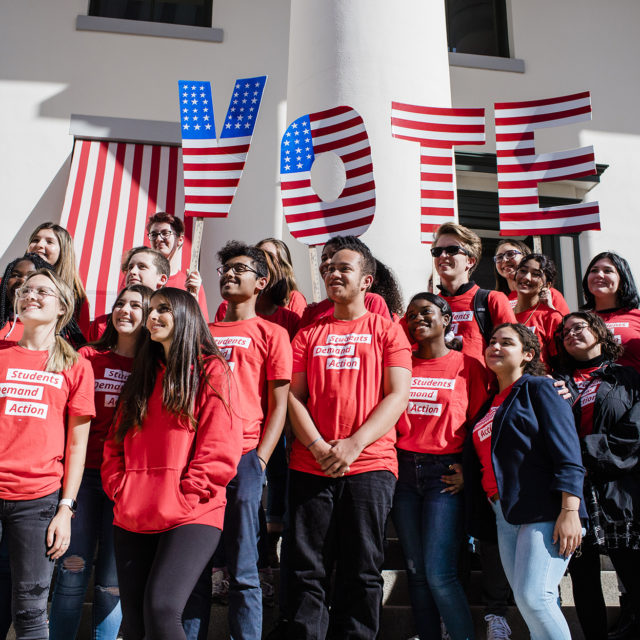 A group of about 20 Students Demand Action volunteers stand with a large VOTE sign