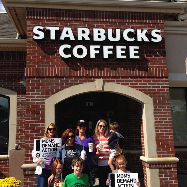 A few Moms Demand Action volunteers hold signs in front of Starbucks