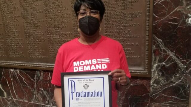 Jenevia Blanks holding a framed proclamation from the Office of the Mayor