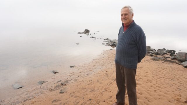 A man, the Sujata's father-in-law, stands on a beach smiling