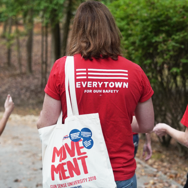 The backs of three volunteers. All three volunteers are wearing Moms Demand Action t-shirts while volunteering to help get out the vote. The volunteer in the middle carries a tote bag that says Movement.