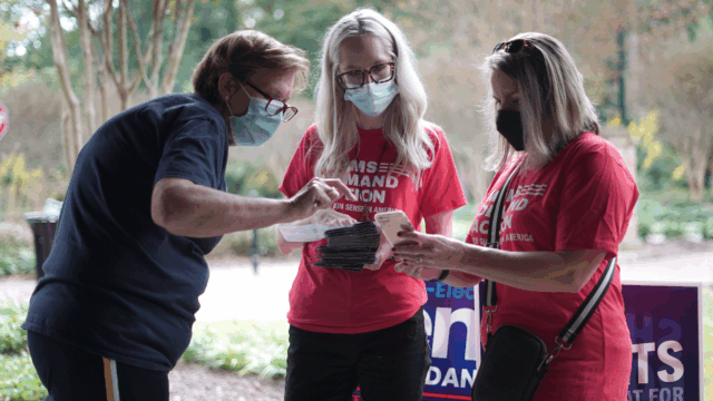 Three volunteers wearing masks look at a stack of pamphlets