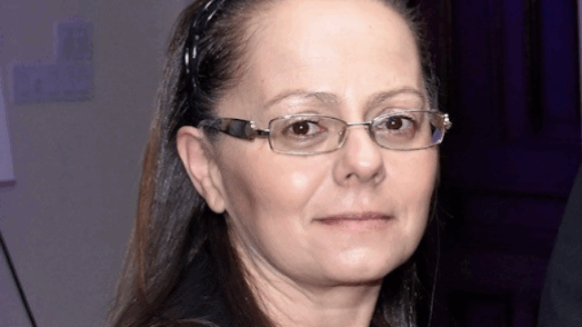 Wendy Linsalata, LIADV Executive Director, poses for a portrait. She wears rectangular glasses with a metal frame, a black blazer, and a maroon blouse. Her straight dark hair is pulled back with a black headband.